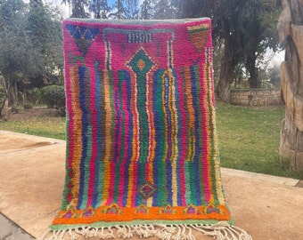 May include: A colorful Moroccan rug with a geometric pattern and fringe. The rug is made of wool and has a variety of colors, including pink, green, blue, and orange.