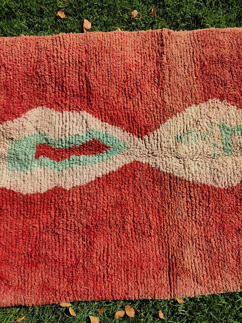 Puede incluir: Una alfombra roja y blanca con un dise&ntilde;o verde. La alfombra tiene una textura suave y est&aacute; hecha de lana.
