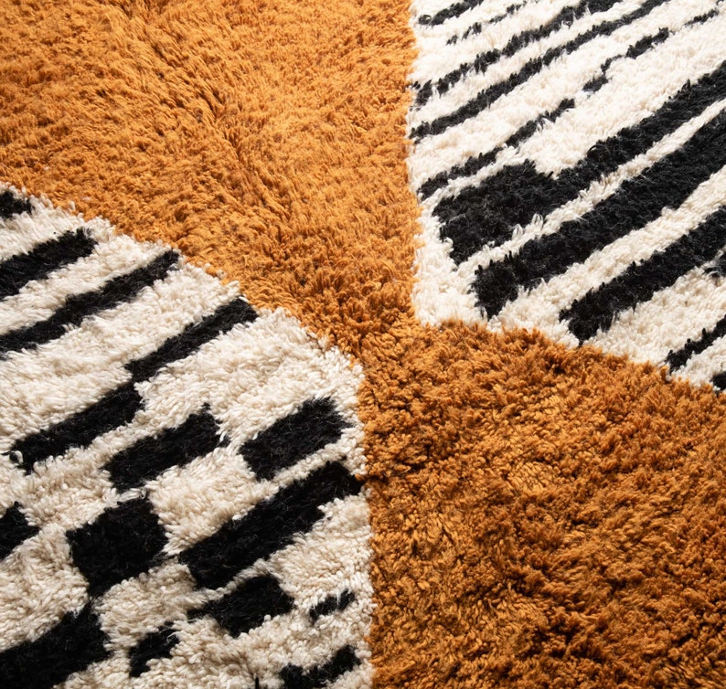 May include: A close-up of a brown, white, and black patterned rug. The rug has a geometric design with stripes and squares.