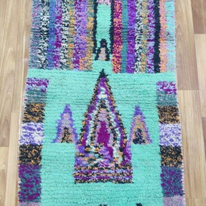 May include: A colourful Moroccan rug with a geometric pattern in shades of purple, pink, orange, and green. The rug has a light green background with a central design of three triangles.