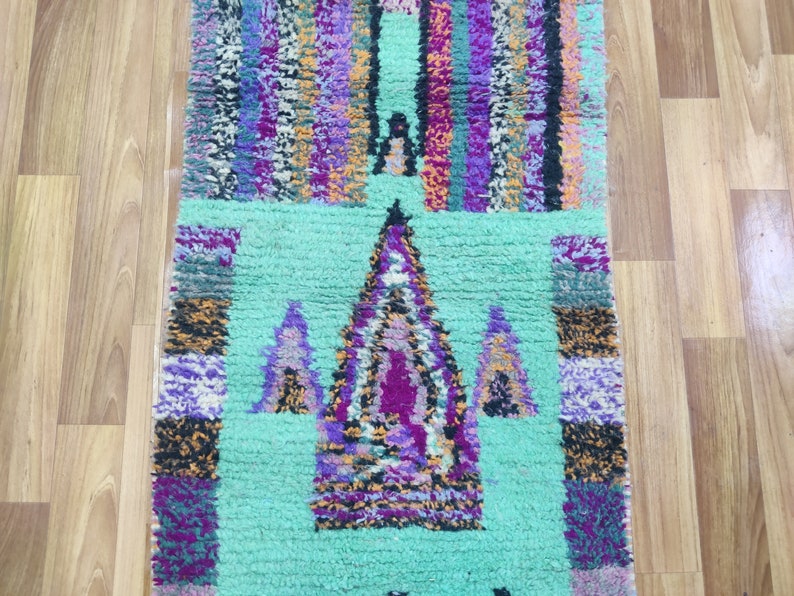 May include: A colourful Moroccan rug with a geometric pattern in shades of purple, pink, orange, and green. The rug has a light green background with a central design of three triangles.