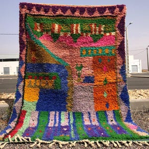 May include: A colorful Moroccan rug with a geometric pattern featuring shades of pink, orange, green, blue, and purple. The rug has a fringe border and is made of wool.