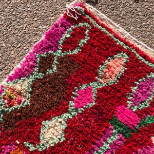 Puede incluir: Una alfombra colorida tejida a mano con un patr&oacute;n geom&eacute;trico en tonos de rosa, rojo, verde y marr&oacute;n. La alfombra tiene un borde de flecos y est&aacute; hecha de lana.