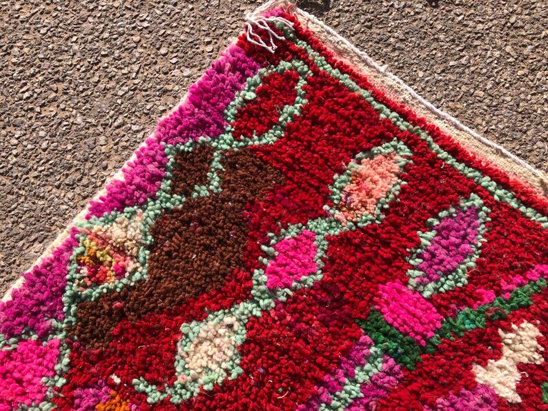 Puede incluir: Una alfombra colorida tejida a mano con un patr&oacute;n geom&eacute;trico en tonos de rosa, rojo, verde y marr&oacute;n. La alfombra tiene un borde de flecos y est&aacute; hecha de lana.