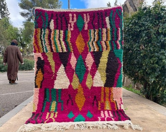 May include: A colorful Moroccan rug with a geometric pattern in shades of pink, green, orange, and white. The rug has a fringe border and is made of wool.