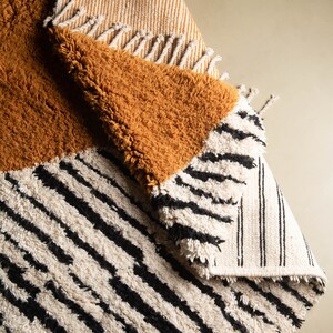 May include: A multi-colored rug with a striped pattern in white and black, a solid mustard yellow section, and a striped section in white and beige.