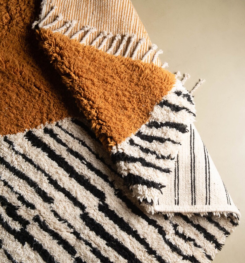 May include: A multi-colored rug with a striped pattern in white and black, a solid mustard yellow section, and a striped section in white and beige.