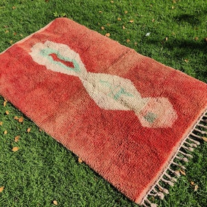 Puede incluir: Una alfombra roja marroqu&iacute; con un patr&oacute;n geom&eacute;trico blanco y verde. La alfombra tiene flecos en los bordes.