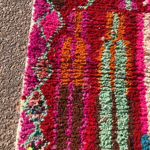 Puede incluir: Primer plano de una alfombra marroqu&iacute; colorida con rayas de color rosa, rojo, naranja, verde, blanco y marr&oacute;n. La alfombra est&aacute; hecha de lana y tiene una textura suave y esponjosa.