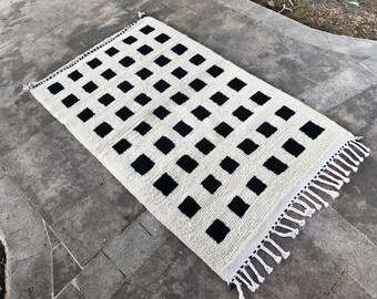 May include: A white rug with a black checkered pattern. The rug has a fringe border.