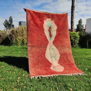 Puede incluir: Una alfombra marroqu&iacute; roja, blanca y verde con un patr&oacute;n geom&eacute;trico. La alfombra est&aacute; colgada de un tendedero en una zona de c&eacute;sped.