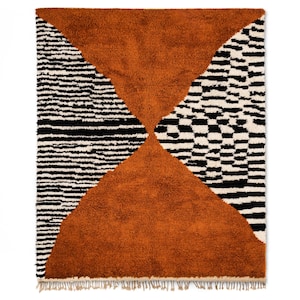 May include: A brown, black, and white geometric patterned rug with a fringe border. The rug has a large, hourglass-shaped brown section in the center.
