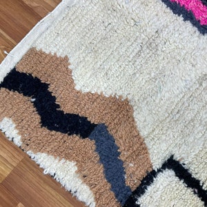 Peut inclure: Un tapis g&eacute;om&eacute;trique &agrave; motifs blancs, bruns, noirs et roses avec une bordure &agrave; franges.