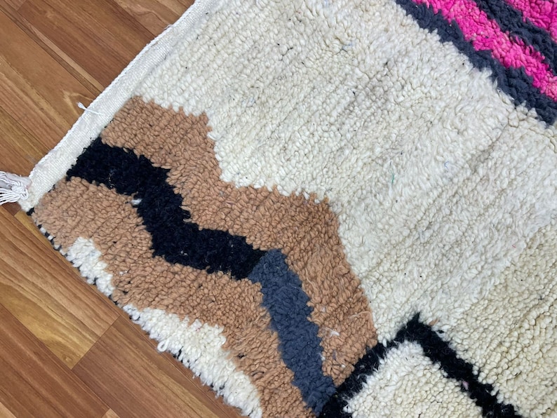 Peut inclure: Un tapis g&eacute;om&eacute;trique &agrave; motifs blancs, bruns, noirs et roses avec une bordure &agrave; franges.