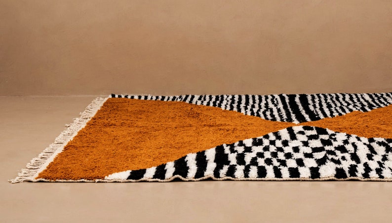 May include: A black, white, and mustard yellow patterned rug with fringe. The rug has a geometric design with stripes, squares, and a large triangle shape.