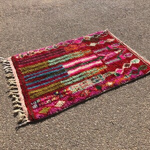 Puede incluir: Una alfombra marroqu&iacute; colorida con un patr&oacute;n geom&eacute;trico en tonos de rosa, rojo, verde, azul y marr&oacute;n. La alfombra tiene un borde de flecos y est&aacute; hecha de lana.