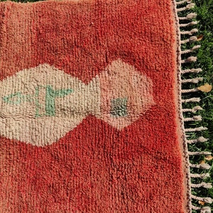 Puede incluir: Una alfombra roja y crema con un dise&ntilde;o geom&eacute;trico. La alfombra tiene flecos en el lado derecho.