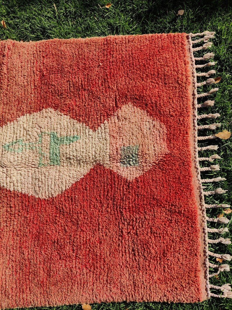 Puede incluir: Una alfombra roja y crema con un dise&ntilde;o geom&eacute;trico. La alfombra tiene flecos en el lado derecho.