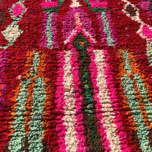 Puede incluir: Primer plano de una alfombra marroqu&iacute; colorida con un patr&oacute;n geom&eacute;trico. La alfombra est&aacute; hecha de lana y tiene una textura suave y esponjosa. Los colores son brillantes y vibrantes, incluyendo rojo, rosa, naranja, verde y blanco.