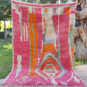 May include: A colorful Moroccan rug with a geometric pattern in shades of pink, orange, green, and white. The rug is hand-woven and has a fringed edge.