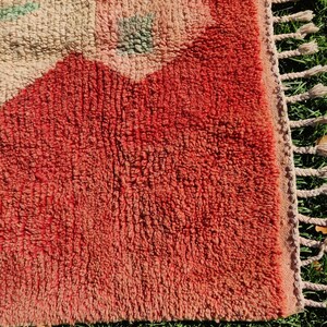 Puede incluir: Primer plano de una alfombra roja y rosa con un patr&oacute;n floral. La alfombra tiene un borde de flecos y est&aacute; hecha de un material suave y esponjoso.