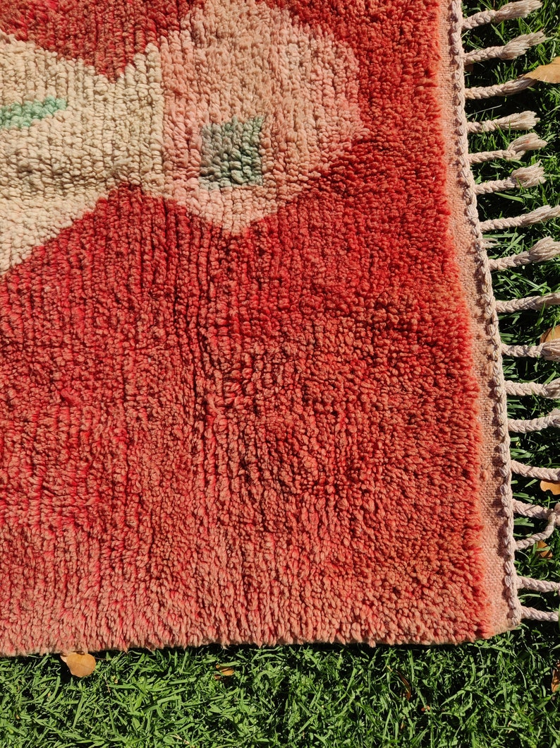 Puede incluir: Primer plano de una alfombra roja y rosa con un patr&oacute;n floral. La alfombra tiene un borde de flecos y est&aacute; hecha de un material suave y esponjoso.