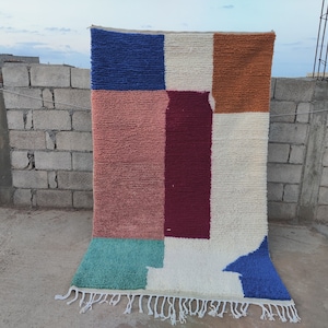 May include: A colorful geometric rug with a white background and blue, red, pink, orange, and green squares. The rug has fringe on the bottom.