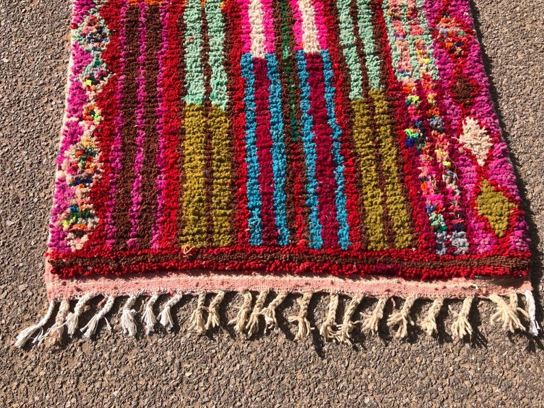 Puede incluir: Una alfombra de rayas coloridas con un borde de flecos. La alfombra est&aacute; hecha de lana y tiene una variedad de colores, incluyendo rosa, rojo, verde, azul y marr&oacute;n.