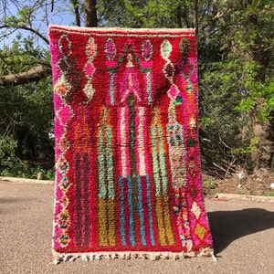 Puede incluir: Una alfombra marroqu&iacute; colorida con un patr&oacute;n geom&eacute;trico en tonos de rosa, rojo, verde, azul y amarillo. La alfombra tiene un borde de flecos y est&aacute; hecha de lana.