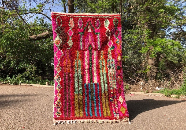 Puede incluir: Una alfombra marroqu&iacute; colorida con un patr&oacute;n geom&eacute;trico en tonos de rosa, rojo, verde, azul y amarillo. La alfombra tiene un borde de flecos y est&aacute; hecha de lana.