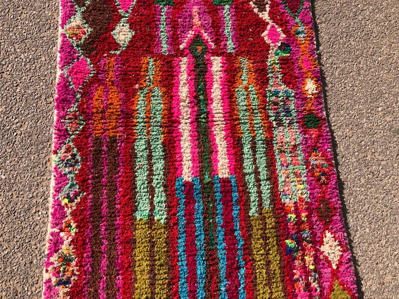 Puede incluir: Una alfombra marroqu&iacute; colorida con un patr&oacute;n geom&eacute;trico en tonos de rosa, rojo, verde, azul y marr&oacute;n. La alfombra tiene un borde de flecos y est&aacute; hecha de lana.