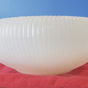 May include: A white, ribbed glass bowl with a rounded shape. The bowl is sitting on a red fabric surface.