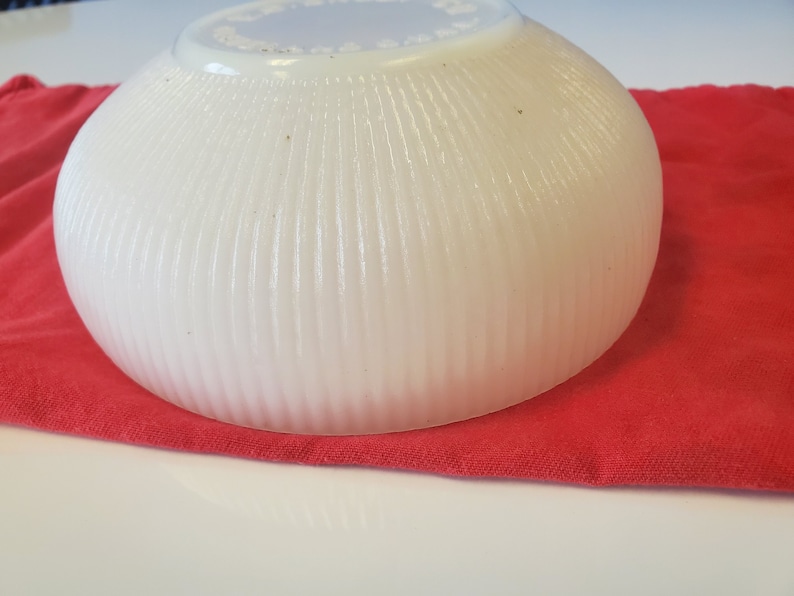 May include: A white, ribbed, ceramic bowl with a scalloped rim. The bowl is sitting on a red cloth.