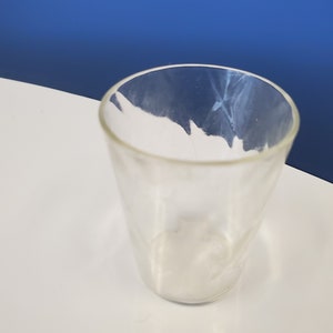 May include: A clear glass shot glass with a slightly textured surface.