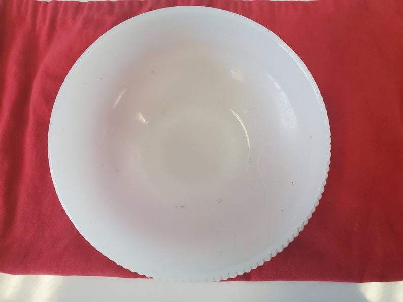 May include: A white ceramic bowl with a scalloped edge. The bowl is empty and has a few small brown spots on the inside.