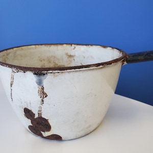 May include: White enamelware pot with a black handle. The pot has rust stains and is chipped in places.