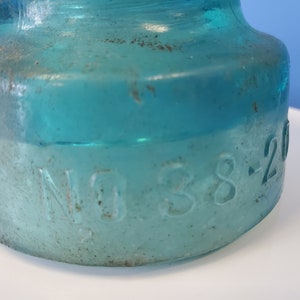May include: Close-up of a teal blue glass insulator with the number "38-20" embossed on the side.