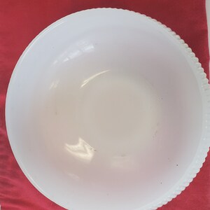 May include: A white, opaque, round mixing bowl with a raised, textured rim. The bowl is made of glass and has a slightly milky appearance.