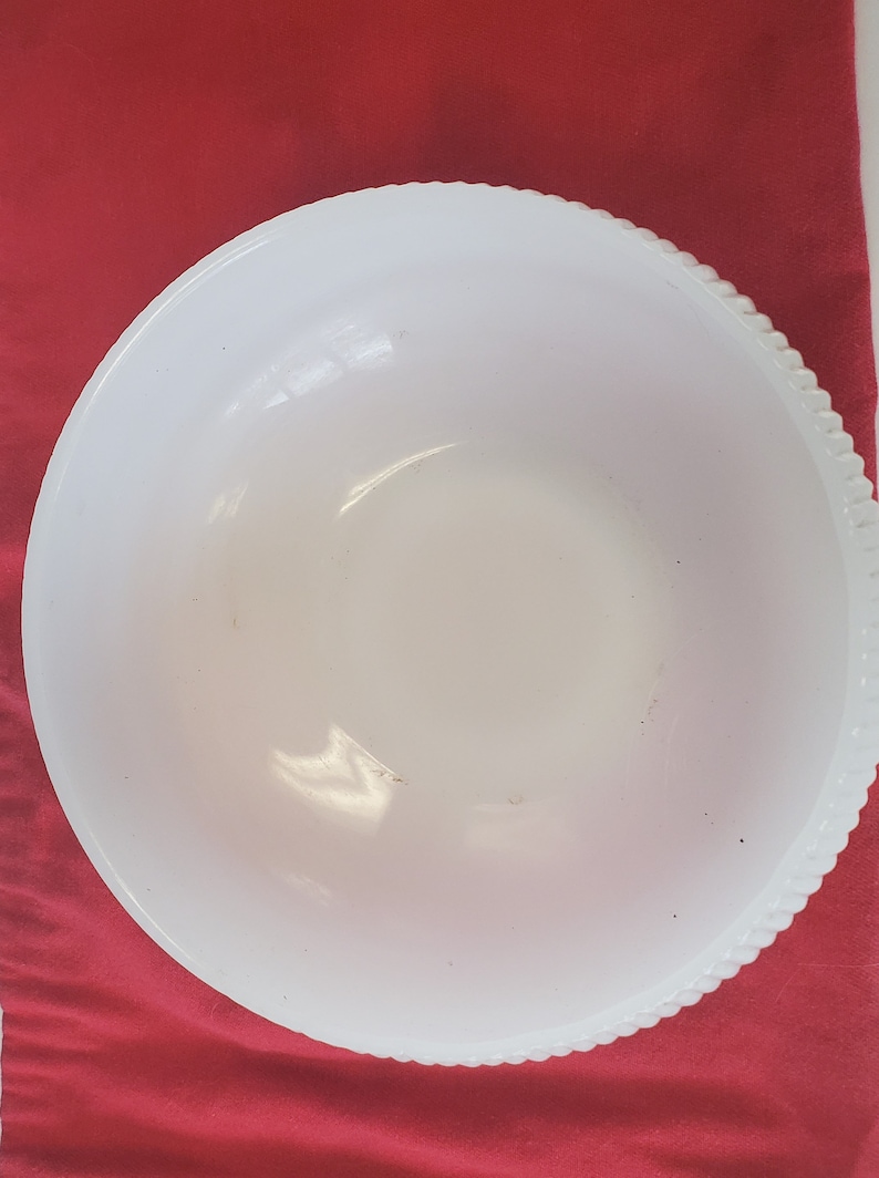 May include: A white, opaque, round mixing bowl with a raised, textured rim. The bowl is made of glass and has a slightly milky appearance.