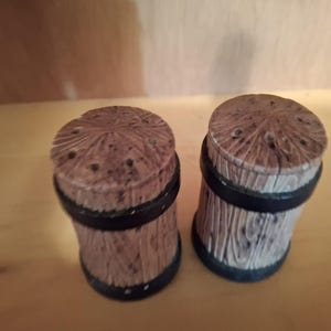 May include: Two brown wooden salt and pepper shakers with black bands around the middle.