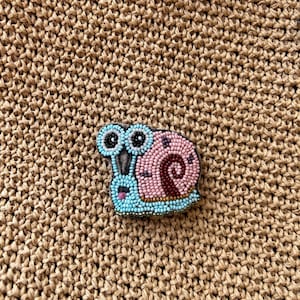 Broche de caracol con cuentas hecho a mano: accesorio inspirado en dibujos animados para bolsos, chaquetas y sombreros. Pin bordado con base de fieltro.
