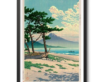 May include: A woodblock print of a Japanese landscape with a mountain in the distance, a beach in the foreground, and two pine trees on the beach. The sky is blue with white clouds. The print is framed in black.