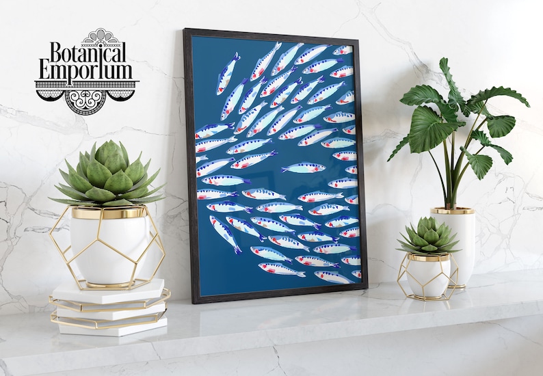 Puede incluir: Una impresi&oacute;n enmarcada de un banco de peces azules y rojos nadando en un fondo azul turquesa. La impresi&oacute;n est&aacute; enmarcada en negro y se encuentra sobre un estante blanco con dos plantas en macetas blancas.