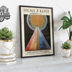 May include: A framed poster of a painting by Hilma af Klint titled "Altarpiece, No. 1". The painting features a black background with a yellow sun and a rainbow-colored pyramid. The poster is displayed on a white marble shelf with two potted plants.