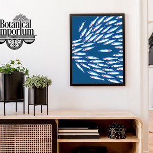 Puede incluir: Una impresi&oacute;n enmarcada de un banco de peces nadando en un fondo azul. Los peces son blancos con acentos azules y rojos. La impresi&oacute;n est&aacute; colgada en una pared blanca sobre un estante de madera.