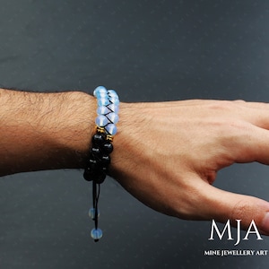 May include: A double-strand bracelet with black and white beads. The white beads are opaque and have a light blue hue. The bracelet has a gold accent and a black cord with a tassel.