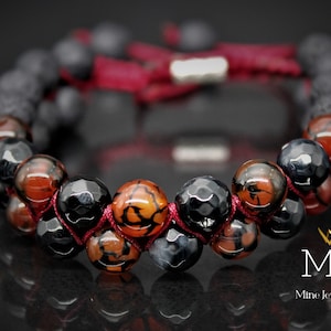 May include: A red and black beaded bracelet with a silver clasp. The beads are made of agate and lava rock. The bracelet is tied with a red cord.