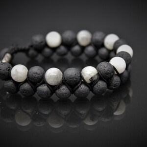 May include: A black and white beaded bracelet with black lava rock and white moonstone beads. The bracelet is made with a black cord and has a knot closure.