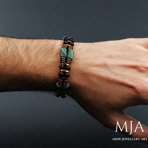 May include: A double-strand bracelet with black and green beads and copper accents. The bracelet is worn on a person's wrist.
