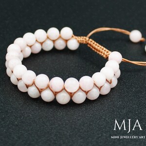 May include: A double-strand bracelet made with pink gemstone beads and brown cord. The bracelet has a sliding knot closure.